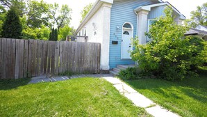 A two-story house with a blue exterior, a wooden fence, and a well-maintained lawn. - Cozy Cove Extension (Winnipeg)