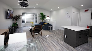A modern living room with a dining area, a kitchen, and a large window with blinds. - Cozy Cove Extension (Winnipeg)