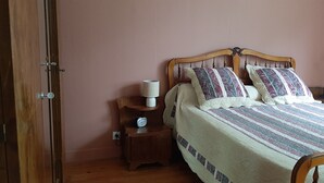 Une chambre à coucher avec un lit en bois, deux oreillers, une table de chevet avec une lampe et une horloge, et une porte.