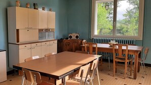 Une pièce avec une table et des chaises en bois, un meuble contenant une radio et une fenêtre donnant sur un paysage verdoyant.