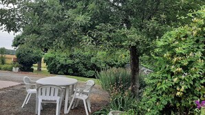 Un espace jardin aménagé avec une table ronde et quatre chaises, entouré d’une végétation luxuriante et de plantes en fleurs.