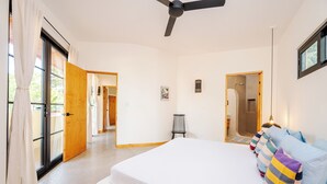 A bedroom with a large bed, a ceiling fan, and a view through an open door.