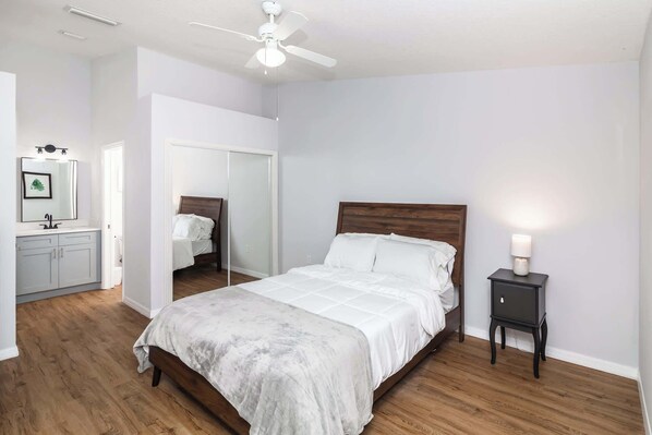 A bedroom with a wooden bed, a bedside table with a lamp, a ceiling fan, and a mirror.