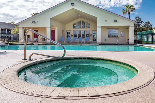 A pool area with a hot tub, lounge chairs, and a building with a covered patio. - Celebrate at Club Cortile (Kissimmee)
