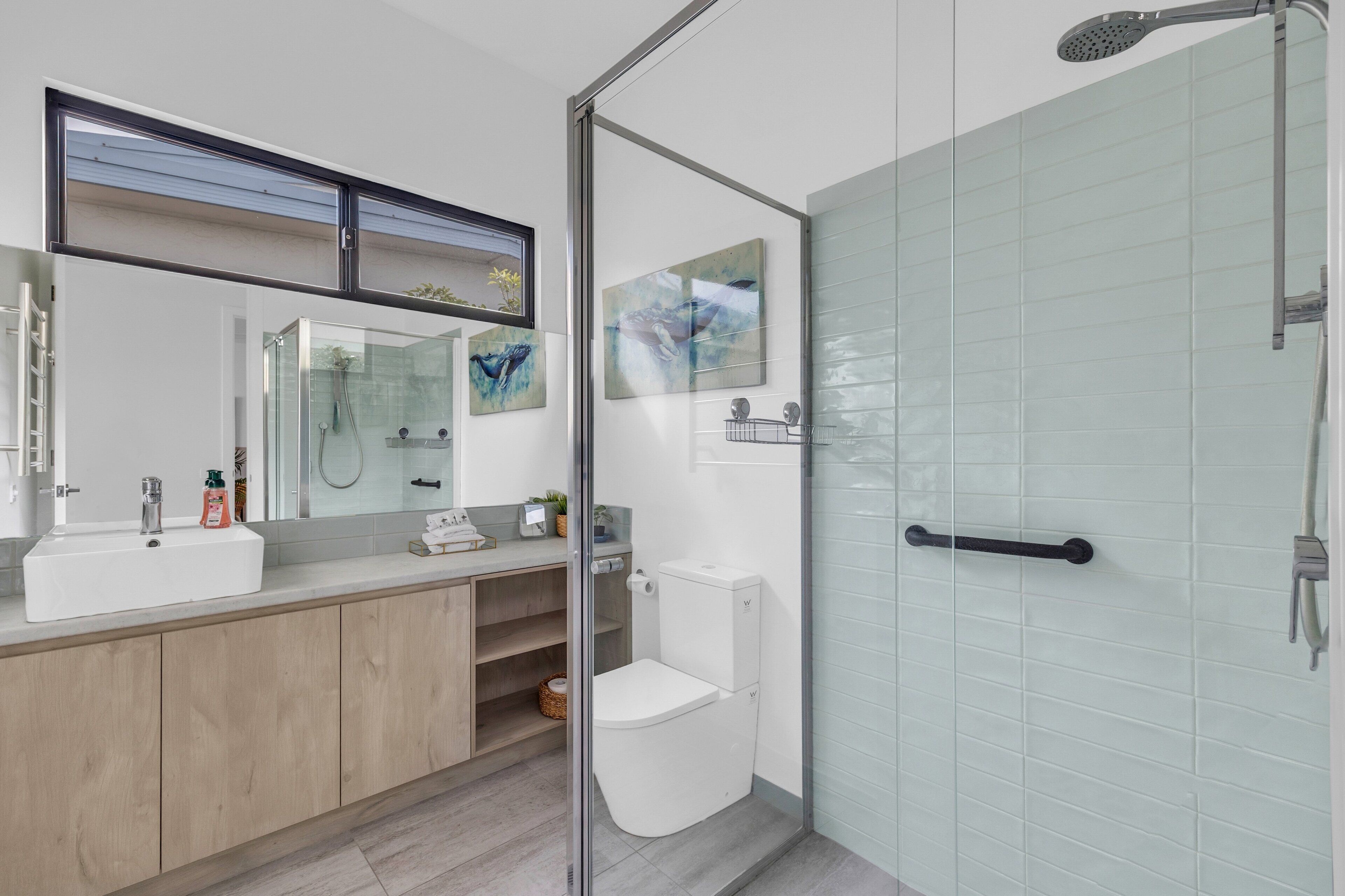 A modern bathroom with a glass shower enclosure, a toilet, and a sink with a mirror above.
