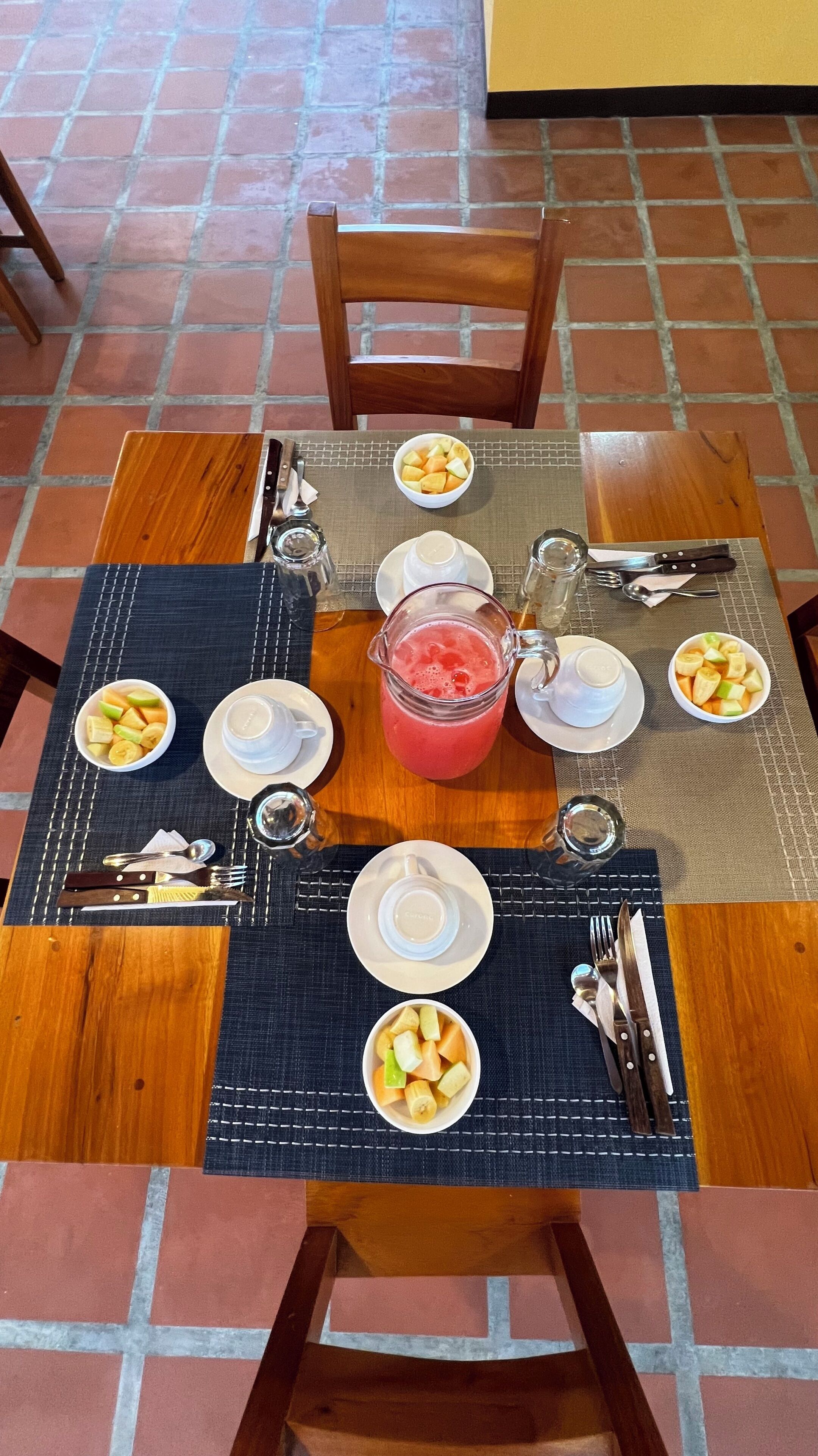 A dining table set with plates, bowls of fruit, a pitcher of juice, and cutlery.