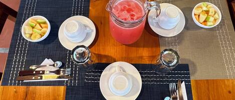 A dining table set with plates, bowls of fruit, a pitcher of juice, and cutlery.