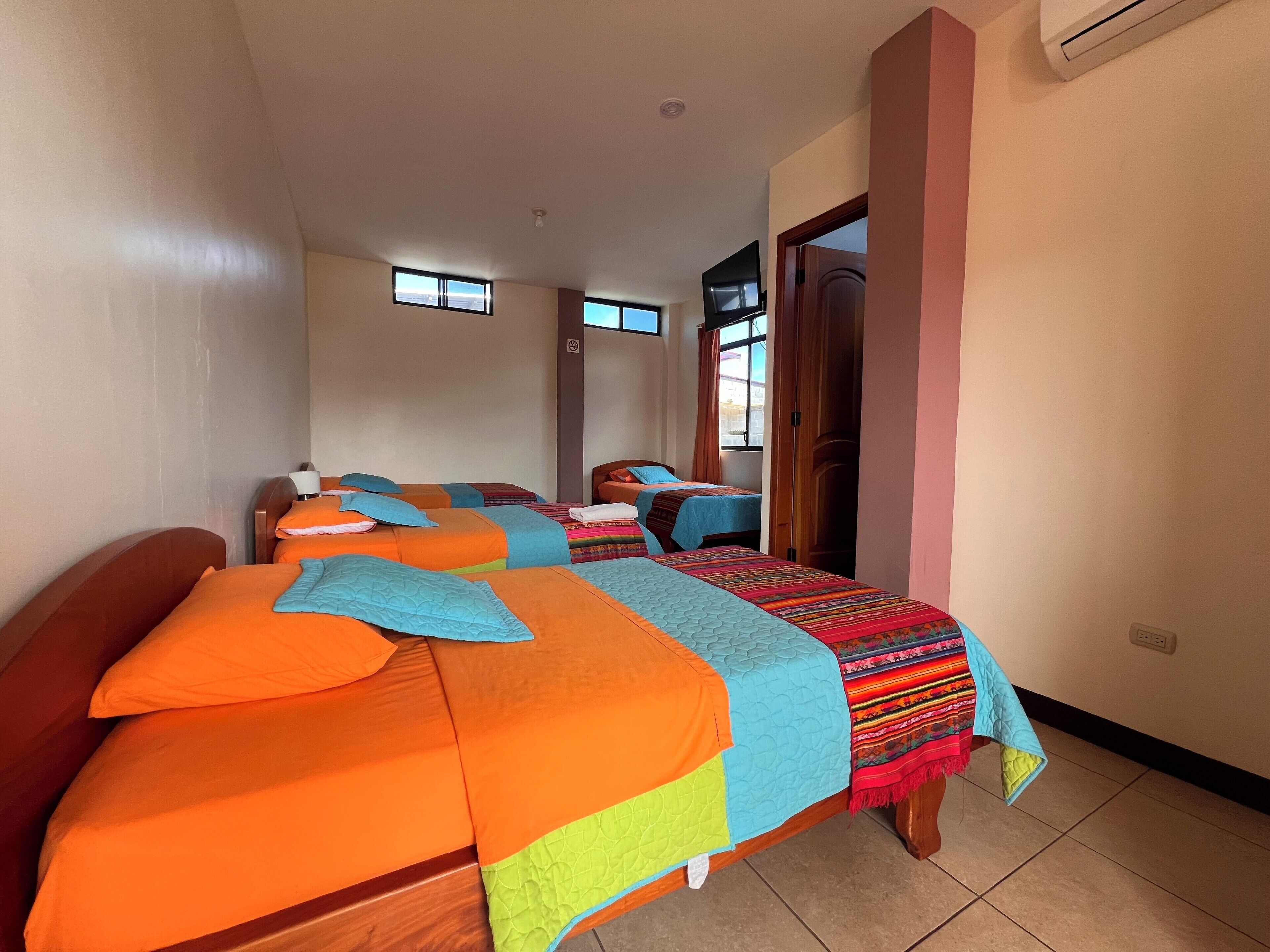 Une chambre d’hôtel avec deux lits, chacun agrémenté d’une literie aux couleurs vives, d’une tête de lit en bois et d’une fenêtre avec des rideaux.
