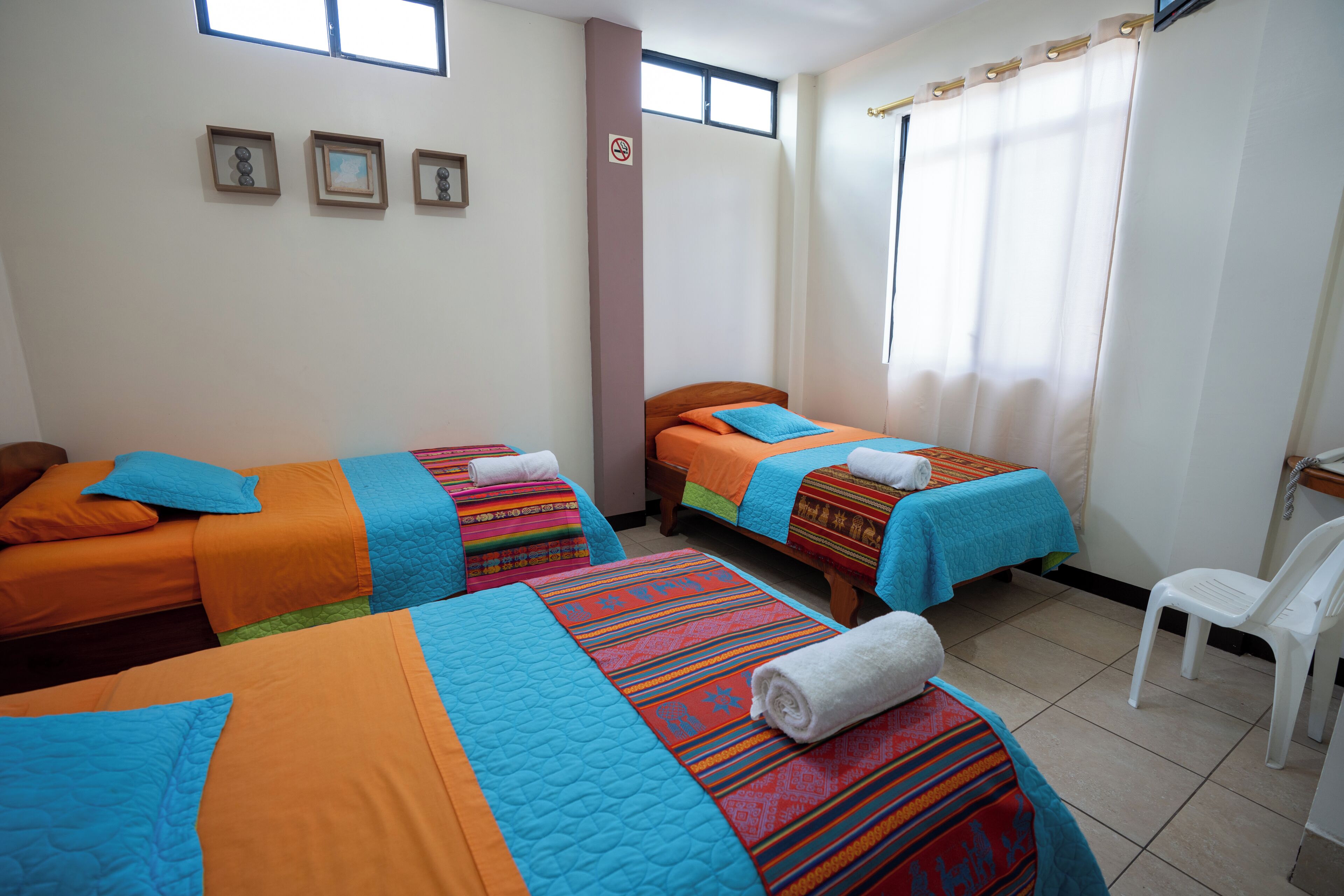 A hotel room with two beds, a chair, and a window with curtains.