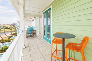 Un balcón con vista a una piscina y palmeras, una mesa con dos sillas y una puerta con ventana.