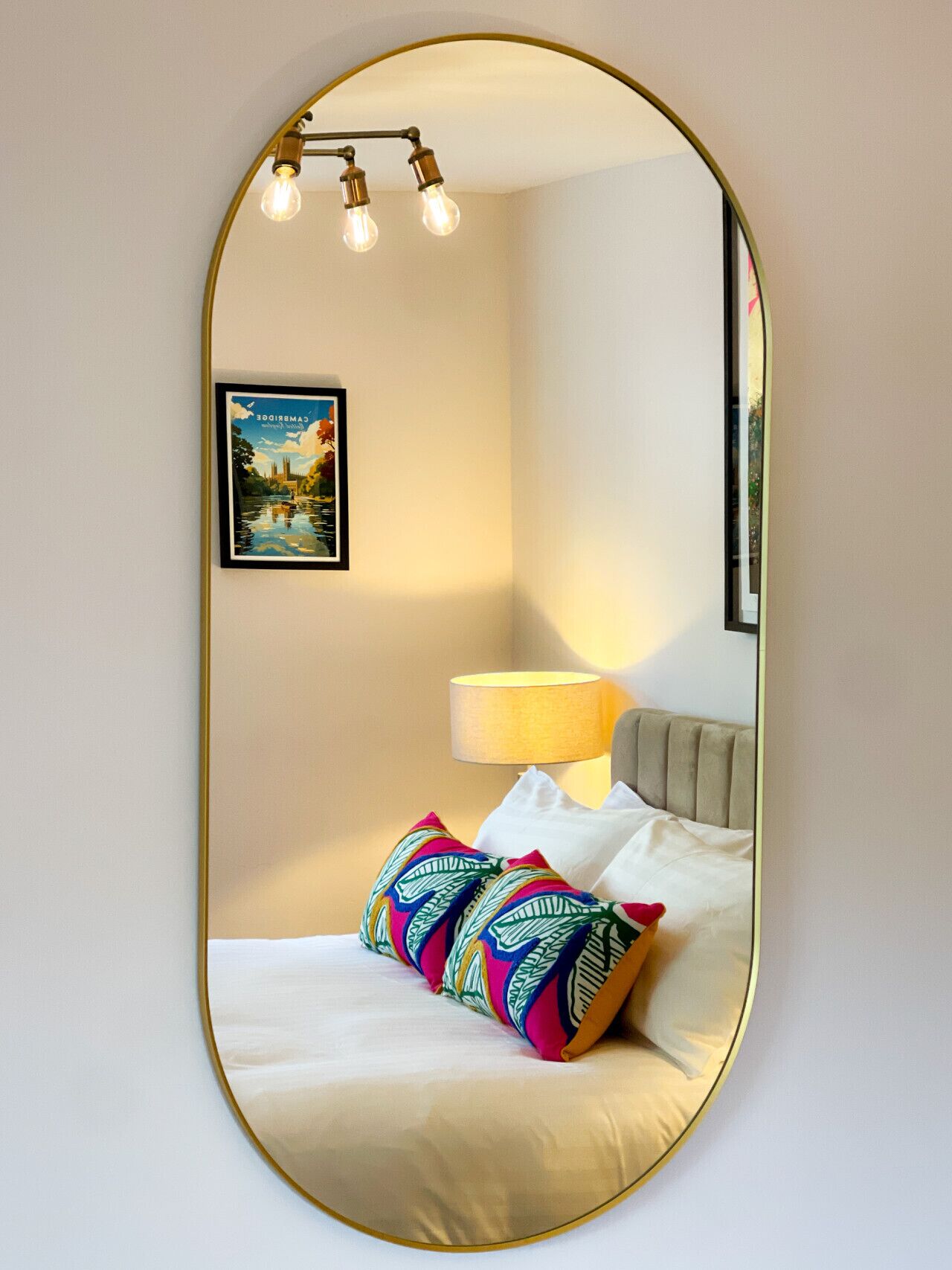 A hotel room with a bed, a bedside lamp, a framed picture on the wall, and a mirror with a gold frame.
