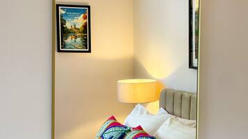A hotel room with a bed, a bedside lamp, a framed picture on the wall, and a mirror with a gold frame.