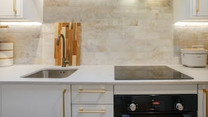 Una cucina moderna con mobili bianchi, un lavello doppio, una schiena di legno e elettrodomestici integrati, tra cui lavastoviglie e forno.