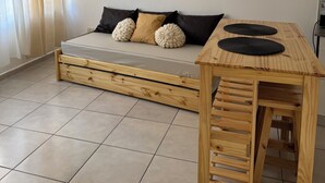 Une pièce au décor minimaliste, avec un lit en bois, une petite table et trois œuvres d’art encadrées accrochées au mur.