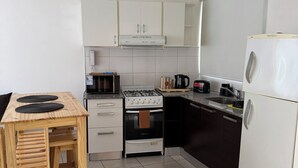 Une cuisine moderne avec des meubles blancs, une table en bois, une cuisinière à gaz, un four encastré, un lave-vaisselle et un réfrigérateur.