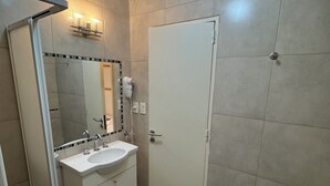 Une salle de bain avec un lavabo blanc, un miroir, une douche et un bidet.