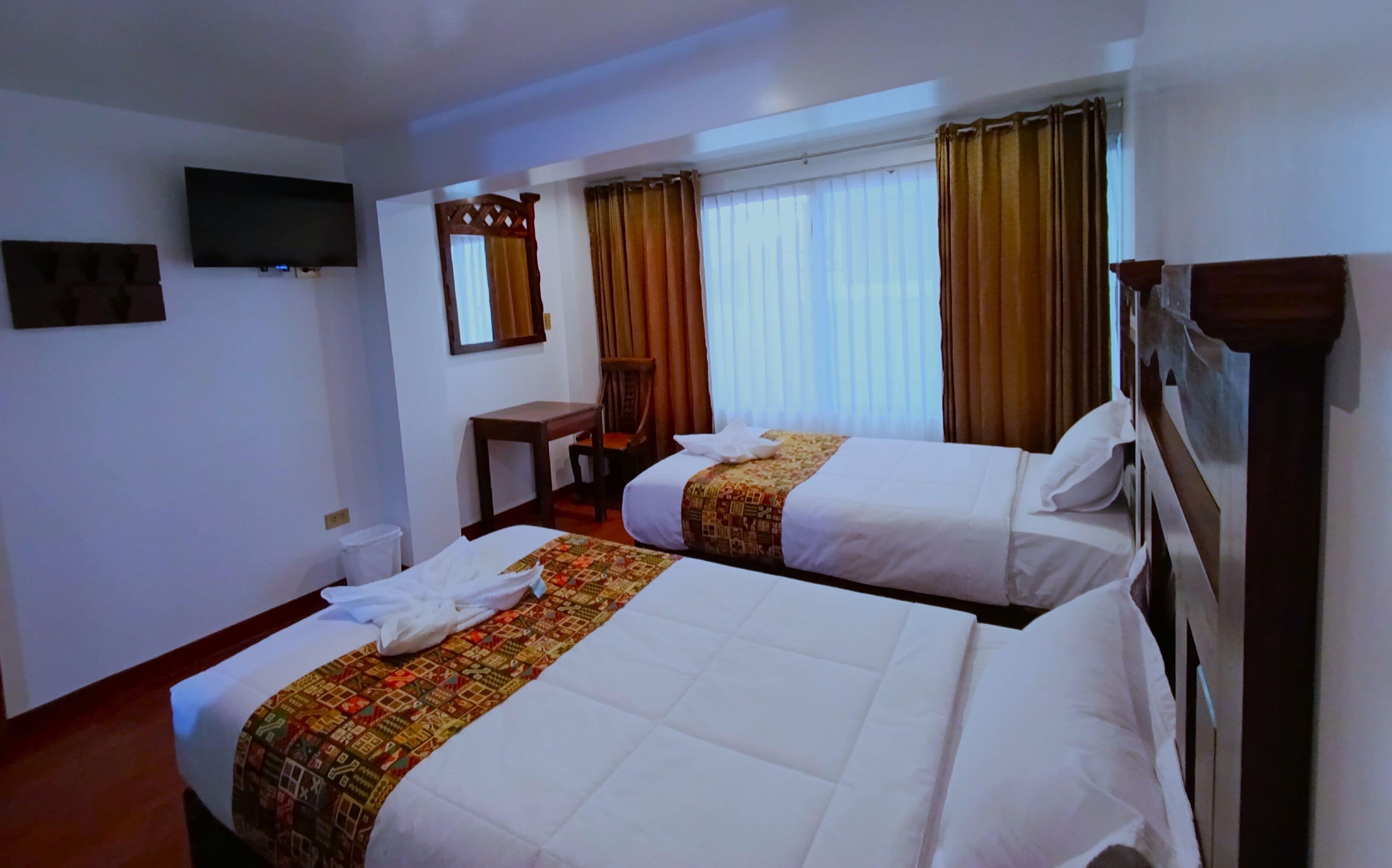 Une chambre d’hôtel avec deux lits, un bureau, une chaise, une télévision et des rideaux.