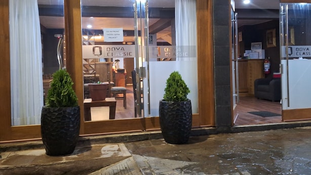L’entrée d’un hôtel, avec une enseigne indiquant « ENTRÉE PRINCIPALE – HÔTEL QOYA PALACE », un comptoir d’accueil et deux plantes en pot.