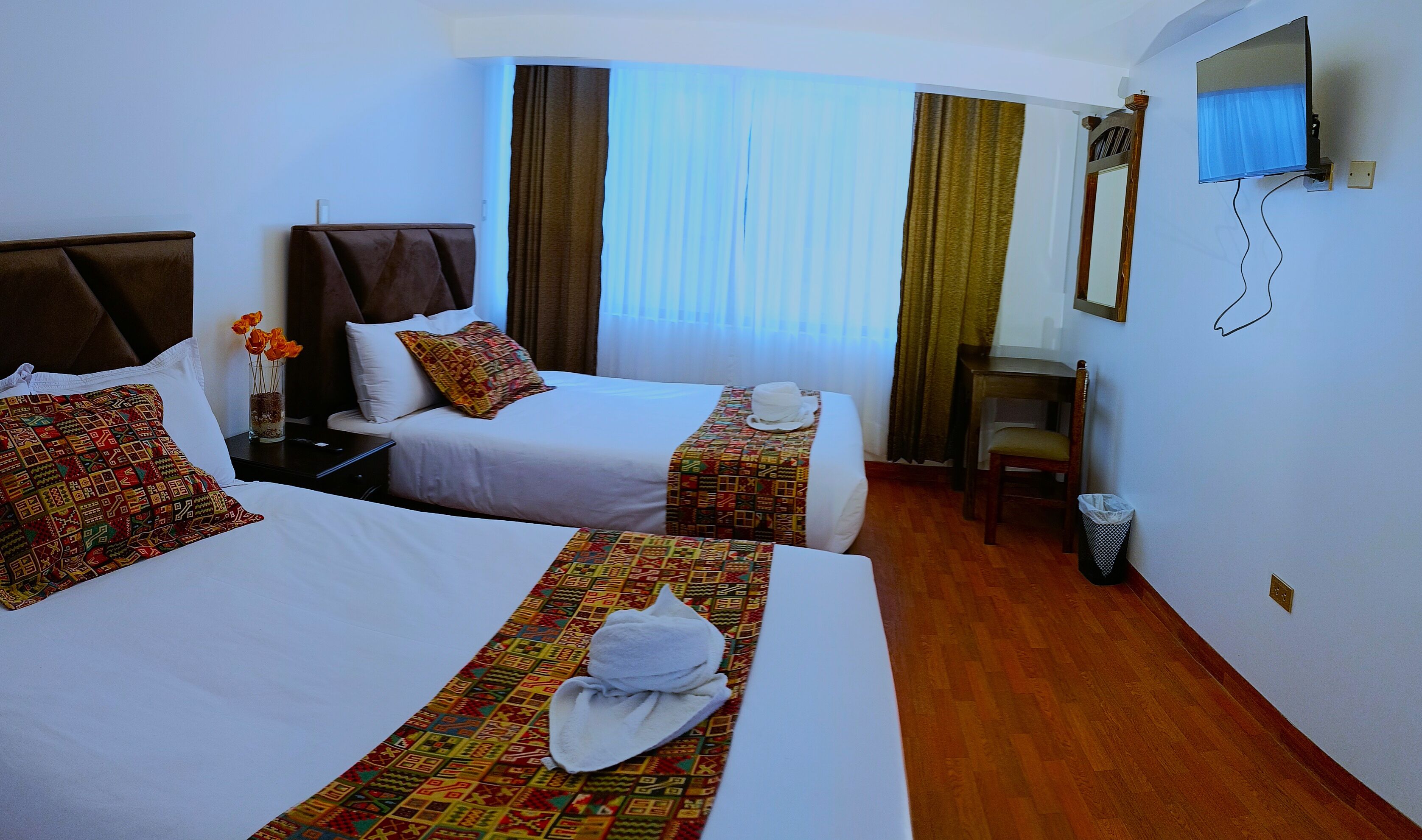 A hotel room with two beds, a desk, a chair, a TV, and a window with curtains.