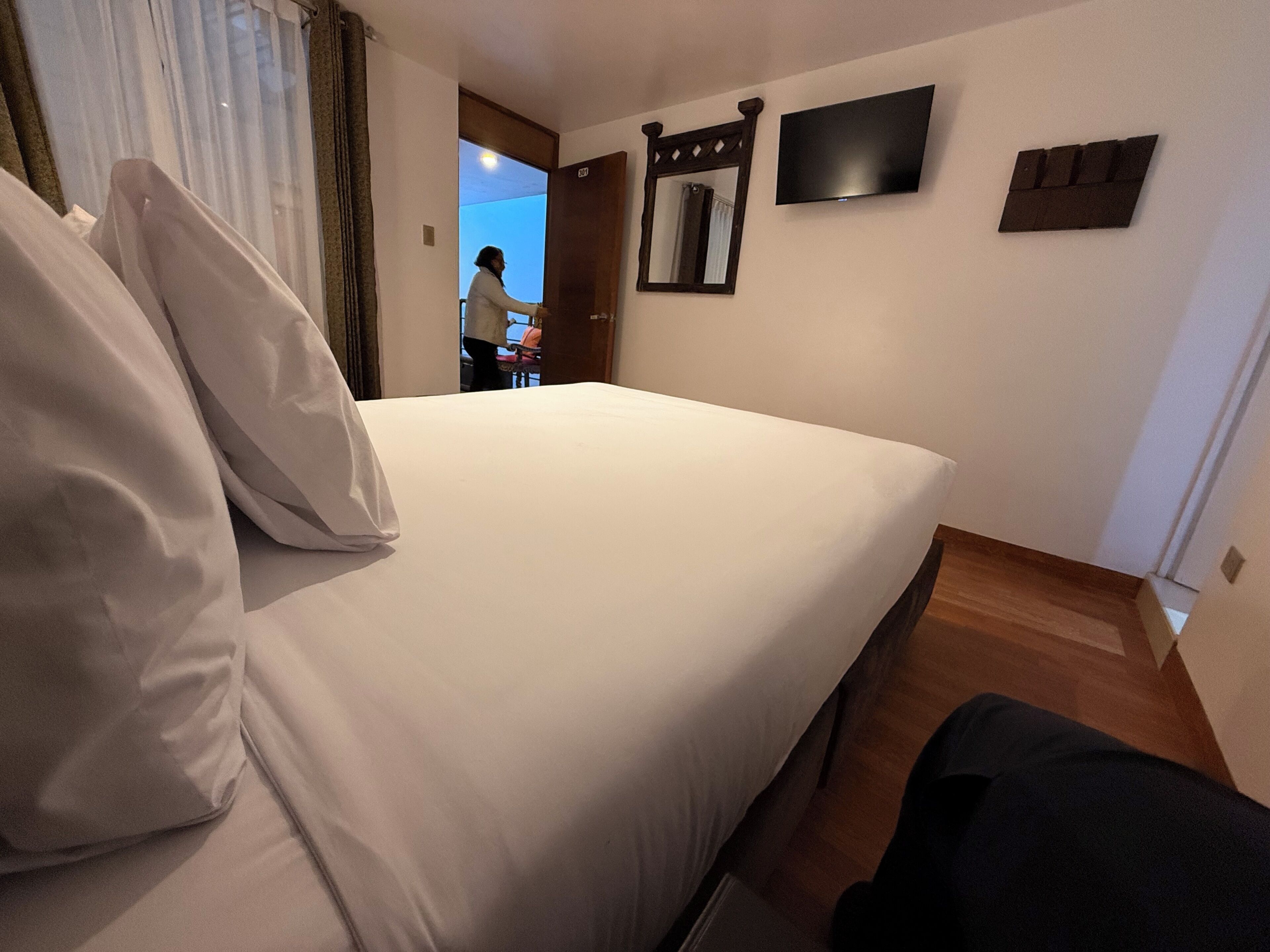 Una habitación de hotel con cama, televisión y puerta que da a otra habitación.