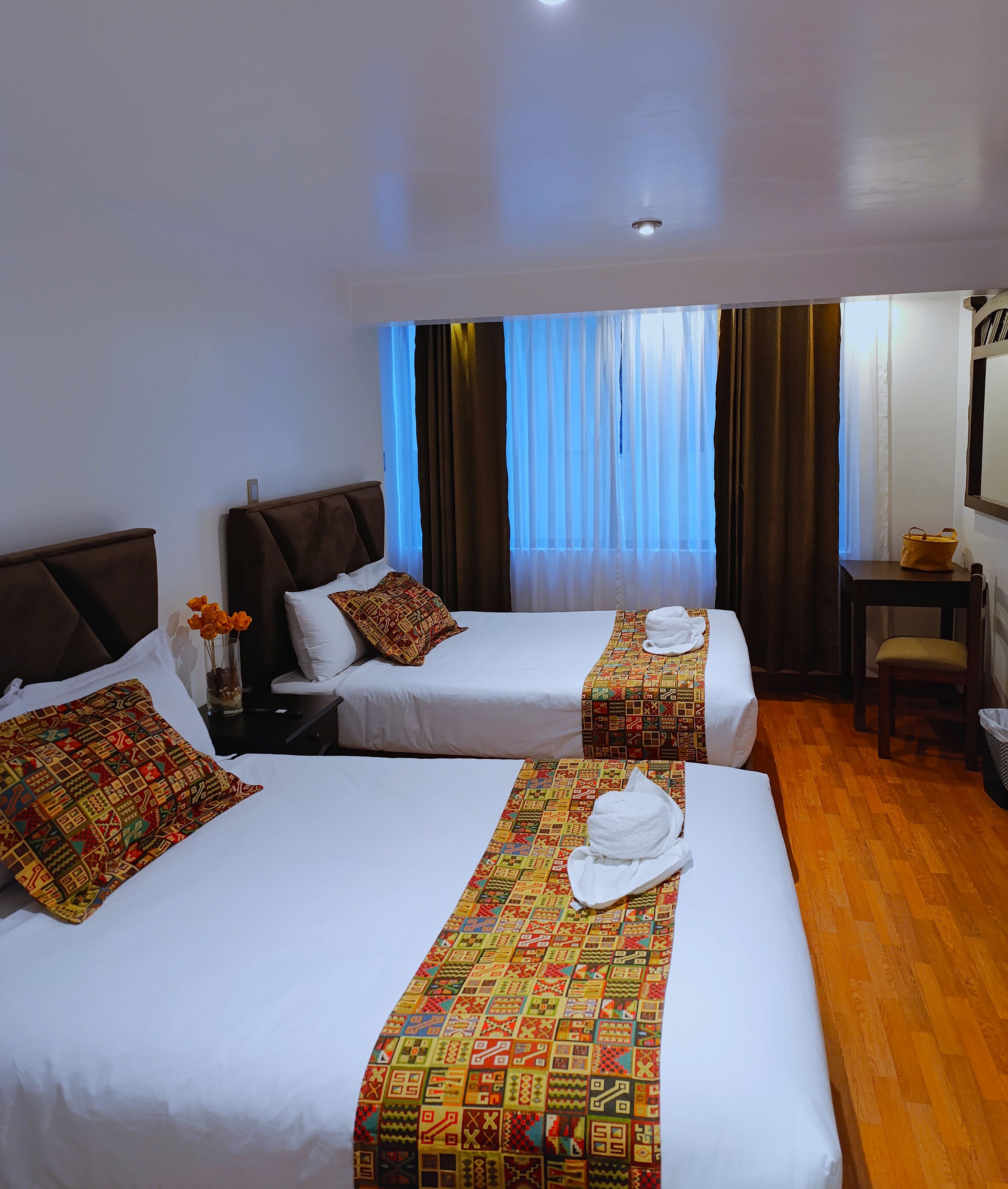 A hotel room with two beds, a wooden floor, a desk, and a chair.