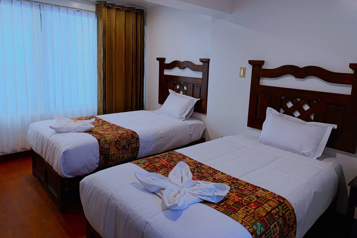 A hotel room with two beds, each with white linens and a colorful blanket.