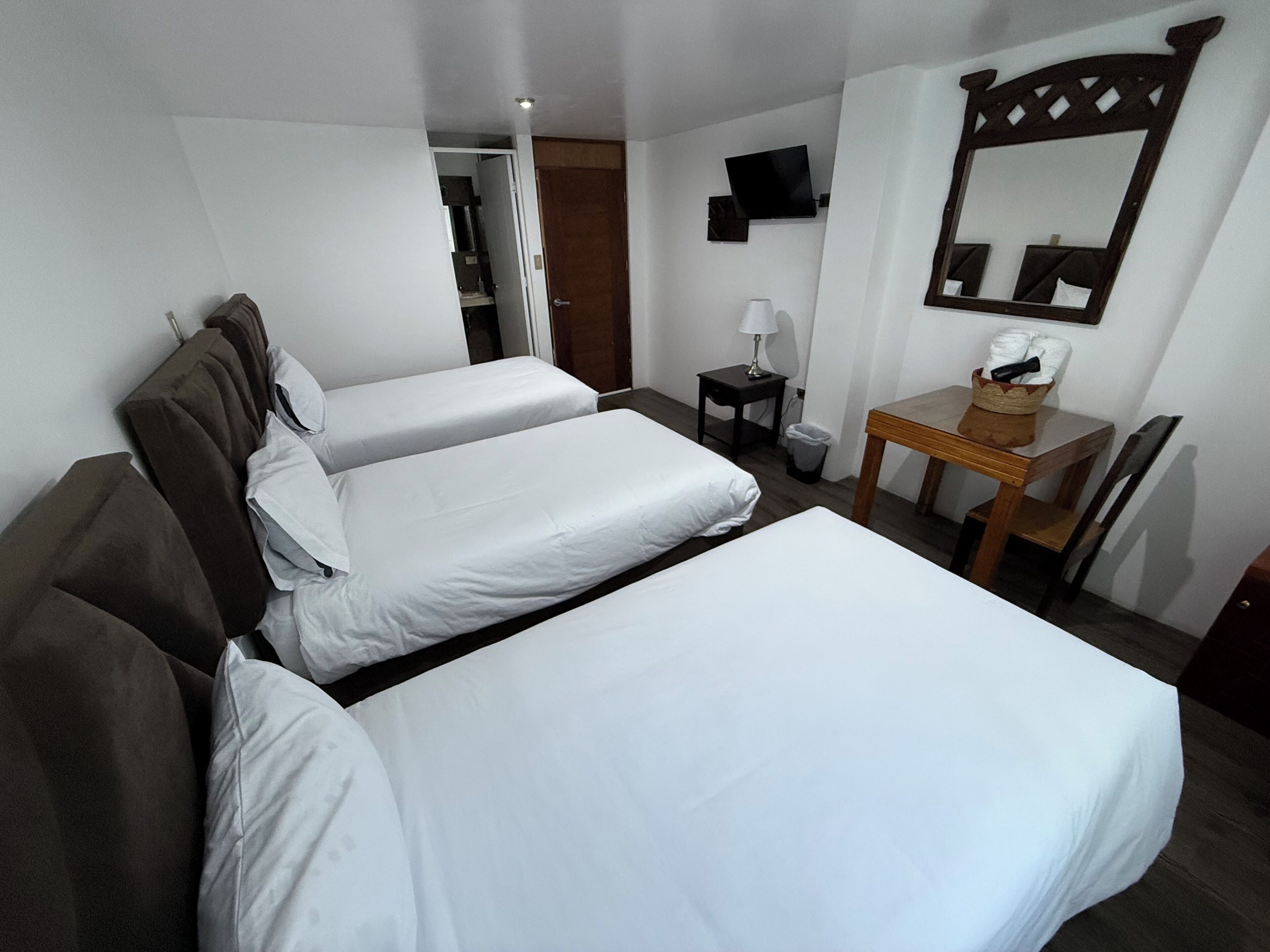 A hotel room with two beds, a small table with a lamp, a chair, a TV, and a mirror.