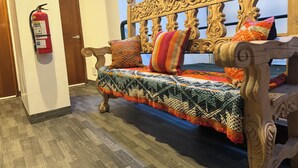 Un banc en bois orné de sculptures complexes, une couverture tricotée aux couleurs vives et un extincteur fixé au mur.