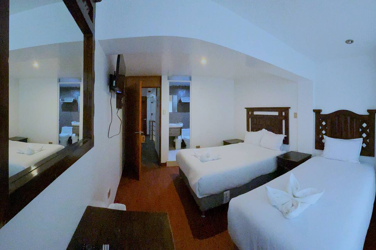 A hotel room with two beds, a large mirror, a wooden headboard, and a small table.