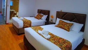 Une chambre d’hôtel avec deux lits, chacun recouvert d’une couvre-lit à motifs et agrémenté d’oreillers, un plancher en bois et une salle de bain visible au fond.