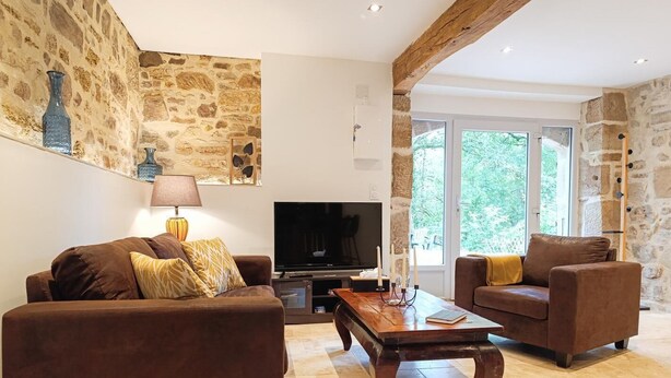 A living room with stone walls, a flat-screen TV, two sofas, a coffee table, and a lamp. - Gîtes de France® - Les Gîtes du Mas de Roujou 1 (LE BOURG)