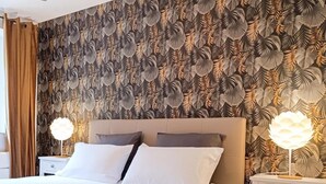 Een hotelkamer met een groot bed, twee nachtkastjes met lampen, een gordijn en behang met een patroon.