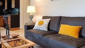 Een woonkamer met een donker leren bank, een glazen salontafel, een lamp en een schilderij aan de muur.