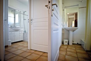 A bathroom with a white sink, mirror, and shower. There is a white door in the foreground.