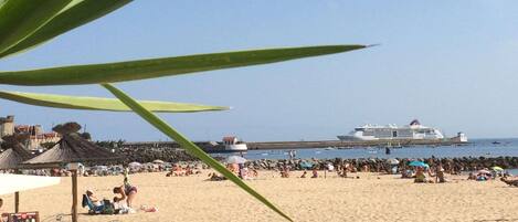A beach with people, umbrellas, and a cruise ship in the background.