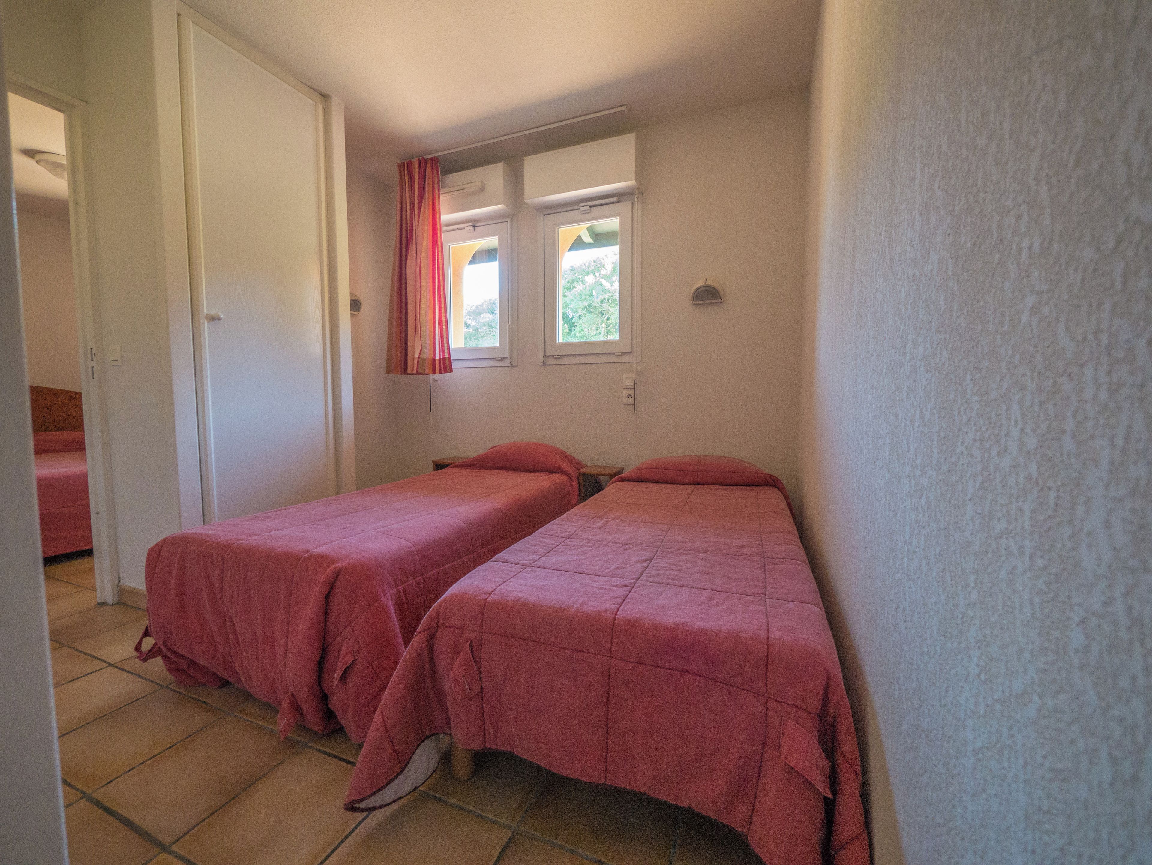 Une chambre avec deux lits, une fenêtre avec des rideaux et une porte.