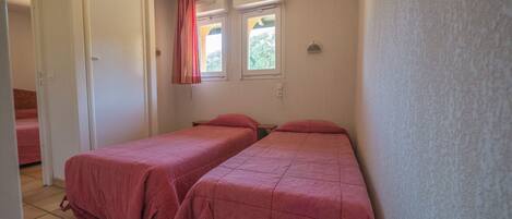 Une chambre avec deux lits, une fenêtre avec des rideaux et une porte.
