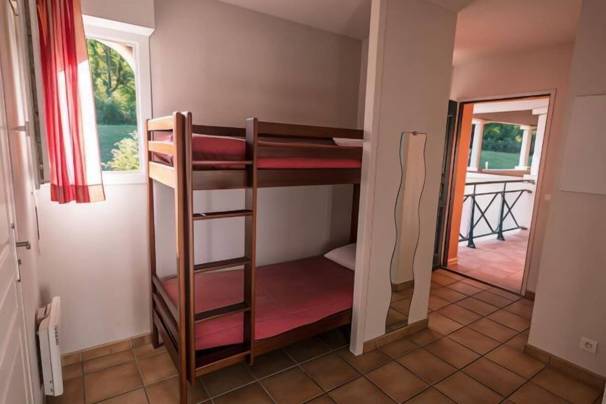 Habitación con literas, ventana, puerta que da al exterior y suelo de baldosas.