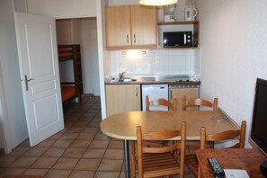 A compact kitchen with a dining table, chairs, a microwave, and a sink. - Résidence Mer & Golf Soko-eder (Ciboure)