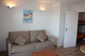A living room with a beige sofa, a small wooden table, and a poster on the wall. - Résidence Mer & Golf Soko-eder (Ciboure)