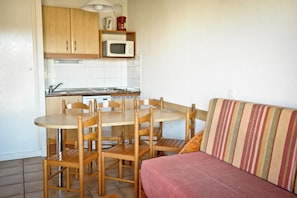 A compact kitchen with wooden cabinets, a microwave, and a dining table with chairs. - Résidence Mer & Golf Soko-eder (Ciboure)