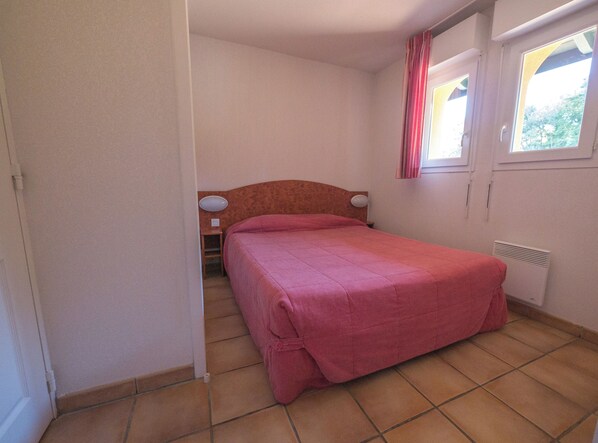 Un dormitorio con una cama individual, una mesita de noche, una lámpara, una ventana con cortinas y un radiador.