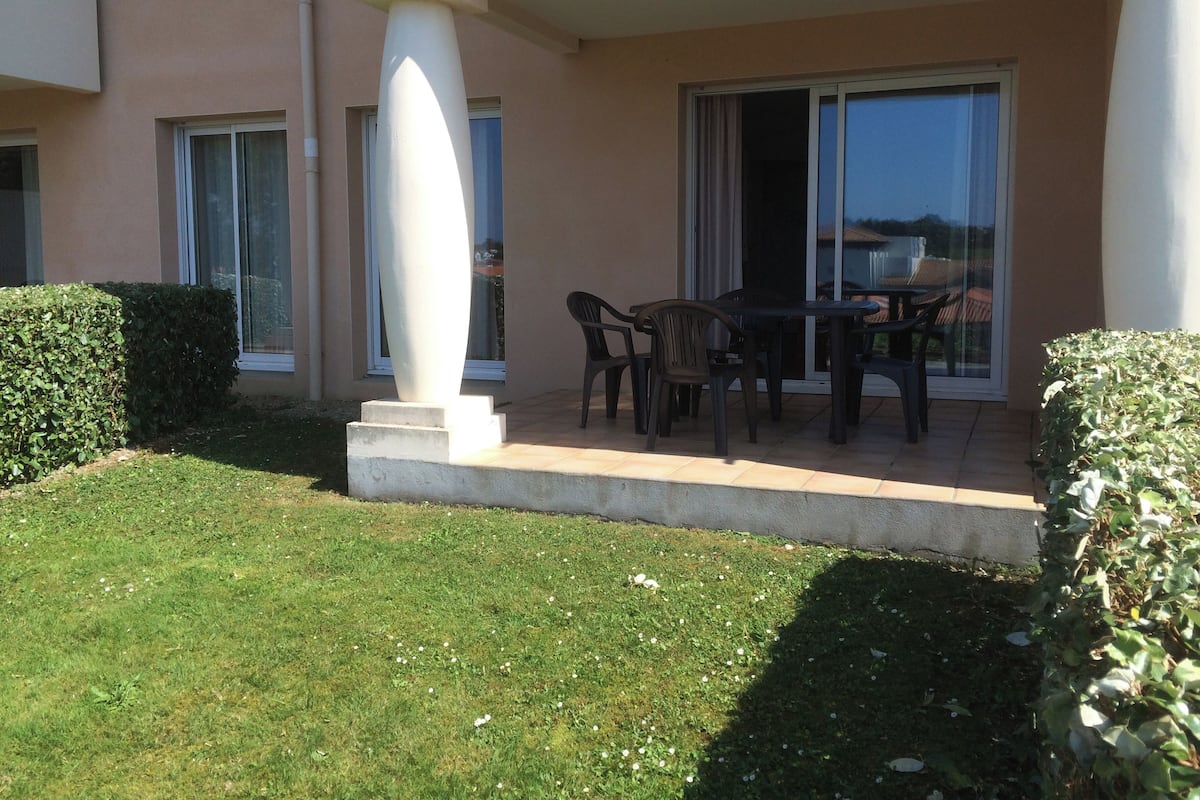 Un patio con una mesa, sillas, una columna blanca y un ventanal de vidrio que da a un balcón.