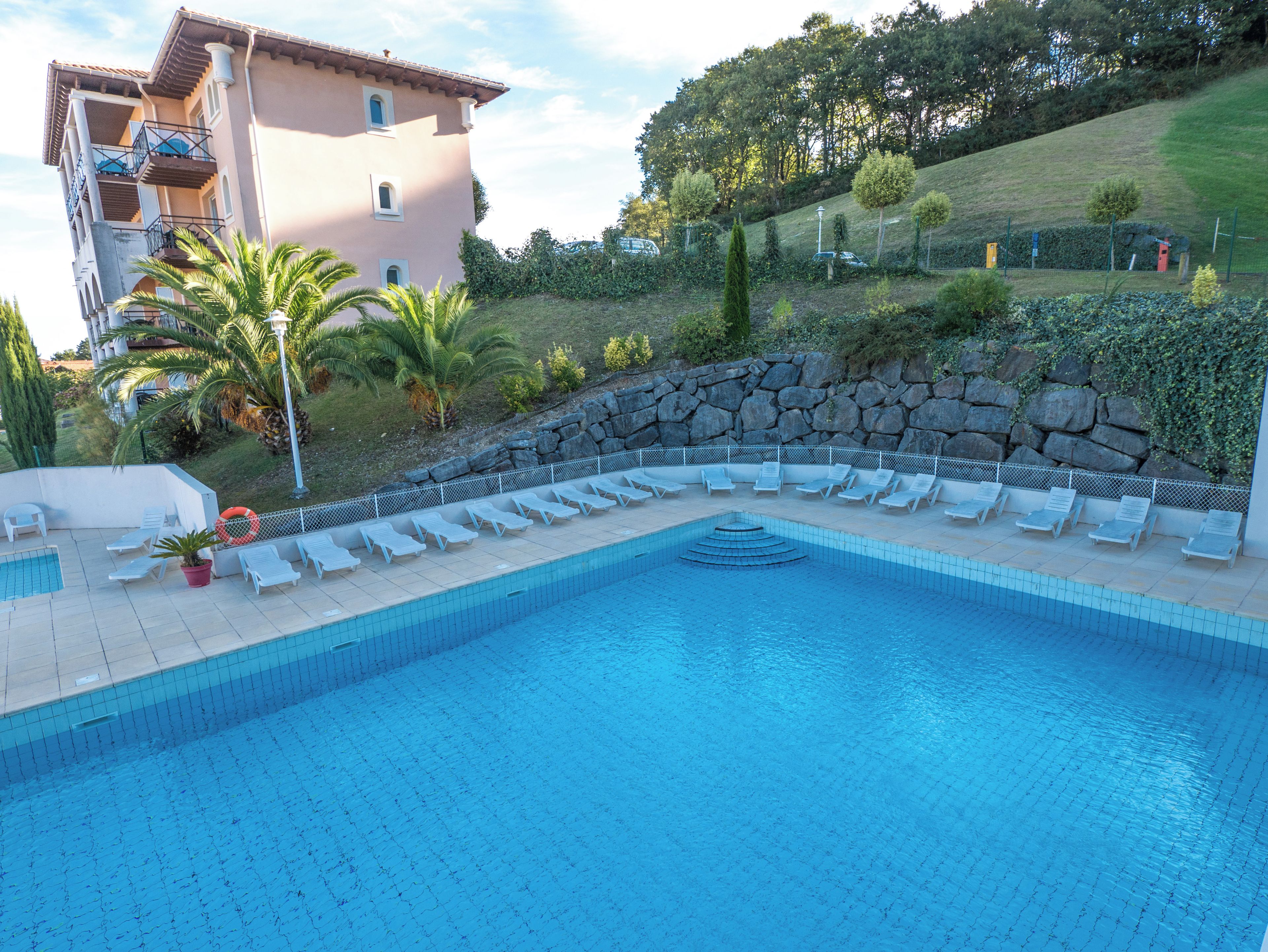 Una piscina con sillas de descanso, un muro de piedra y un edificio con balcones.