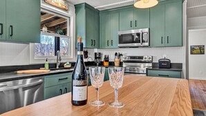 A modern kitchen with teal cabinets, stainless steel appliances, and a wooden island with wine glasses and a bottle. - Charming, fully renovated 19th century cabin with spectacular views. 4 BR, 2 BA. (Arrington)