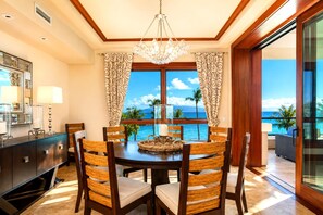 A dining area with a view of the ocean, featuring a chandelier, wooden chairs, and a buffet table.