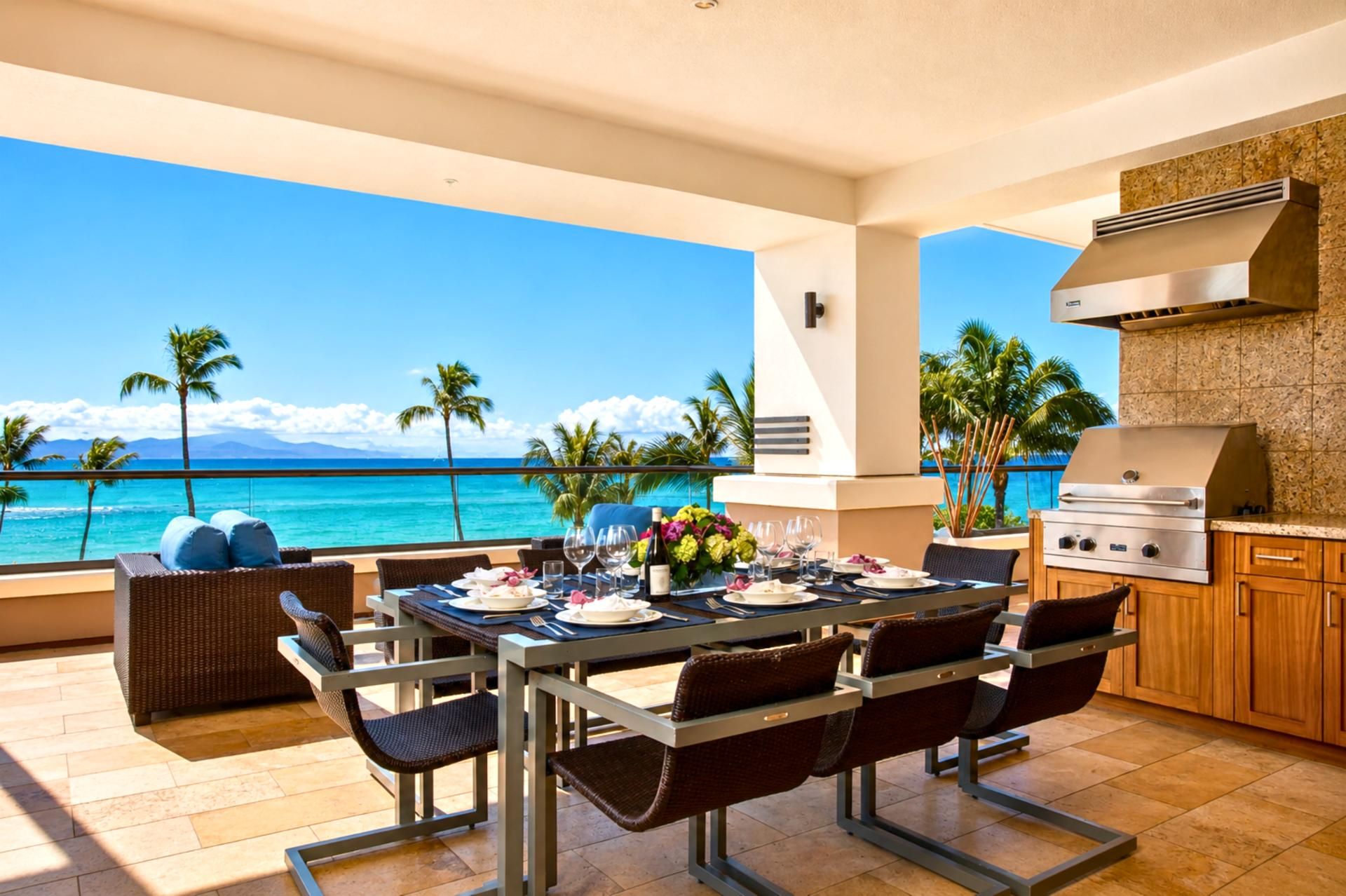 An outdoor dining area with a view of the ocean, a grill station, and a table set for a meal.