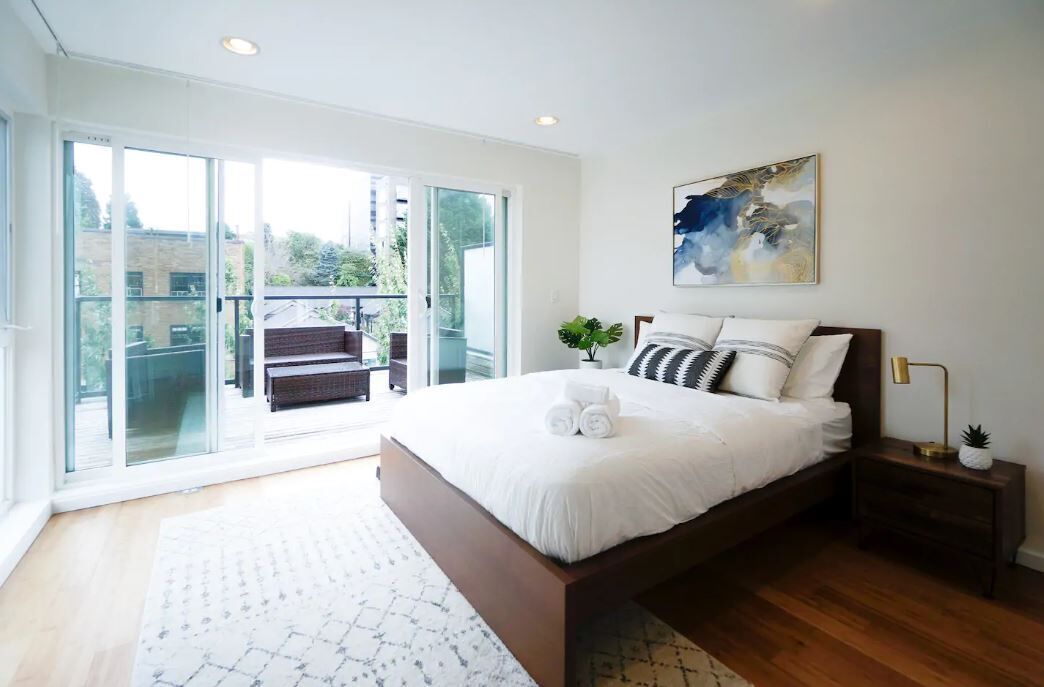 A bedroom with a large bed, a nightstand, a painting, and a view through a glass door to an outdoor area.