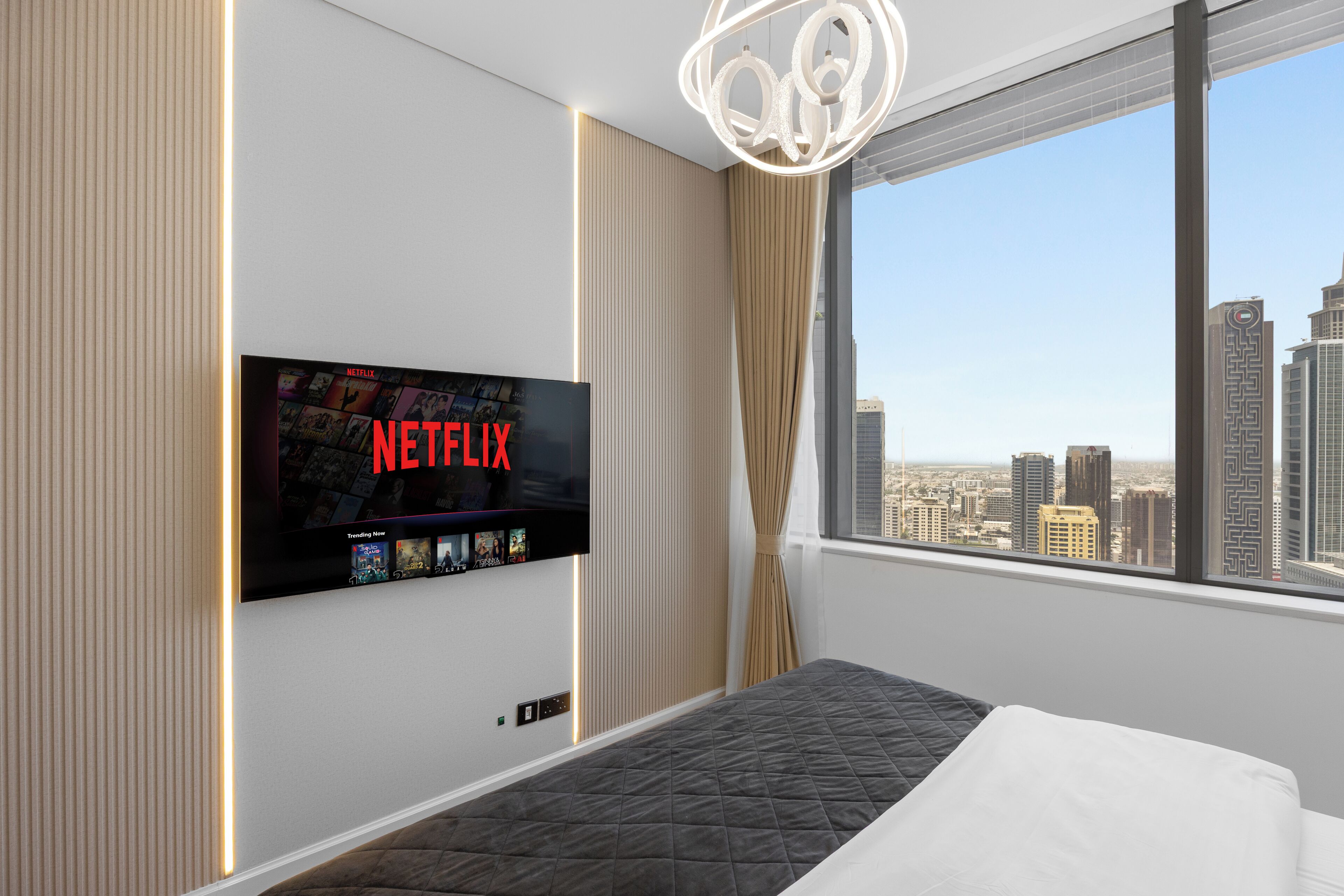 A hotel room with a large window, a bed, a wall-mounted TV displaying the Netflix logo, and a cityscape view.