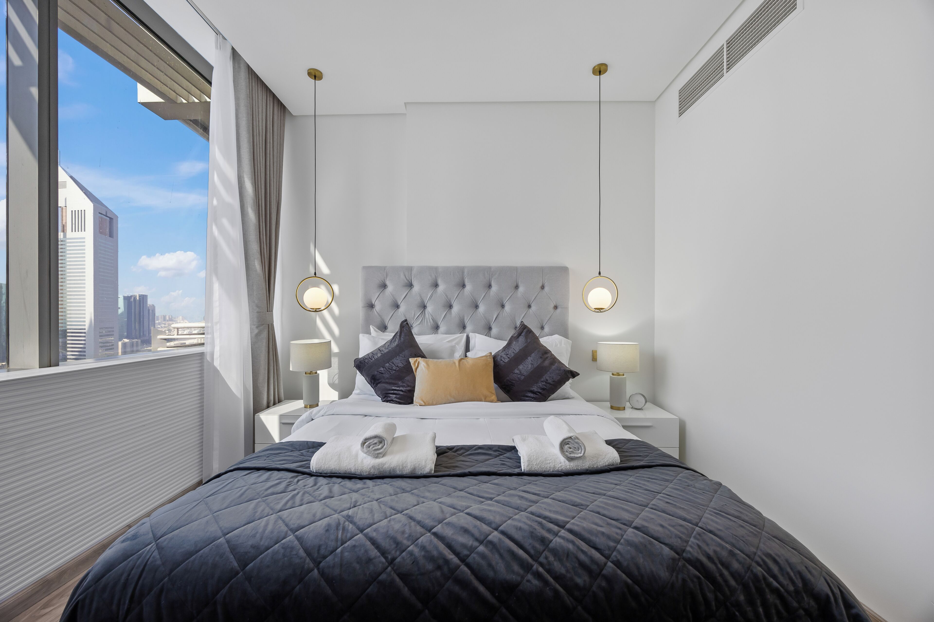 Et moderne hotelværelse med en stor seng, to sengeborde med lamper, udsigt over bybilledet og en silhuet af byens skyline gennem vinduet.
